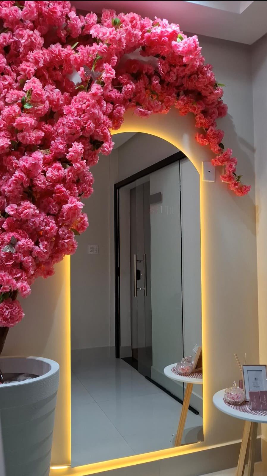 O cantinho do Studio Zoe: espelho em arco pleno emoldurado por flores rosa, com a fita de LED âmbar acesa na borda.